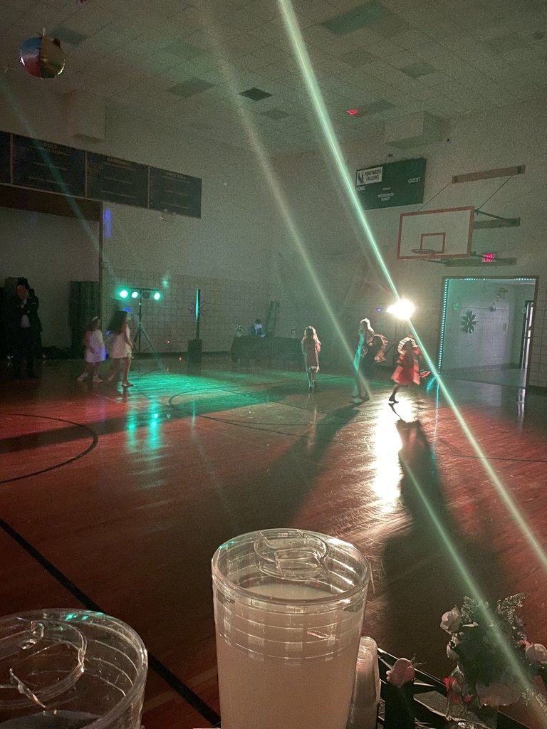 Elementary kids and their families dancing in a dark gym.
