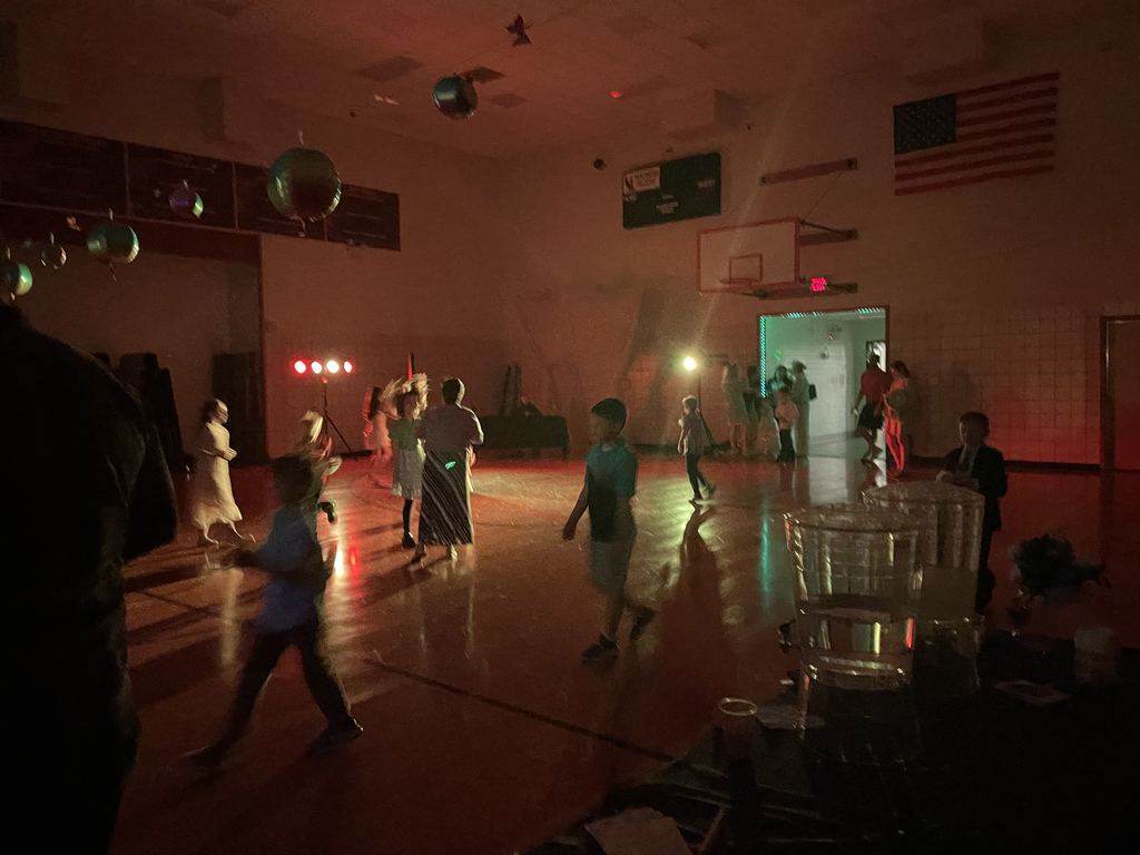 Elementary kids and their families dancing in a dark gym.