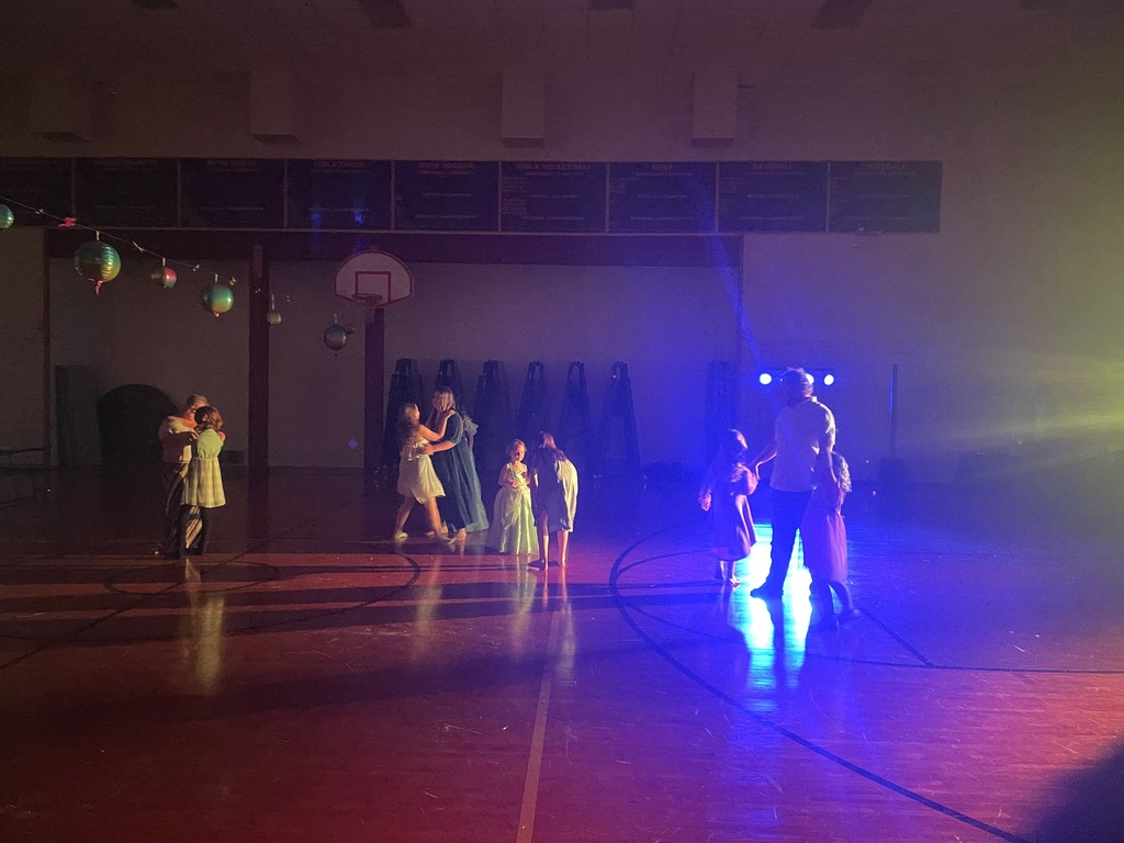 Elementary kids and their families dancing in a dark gym.