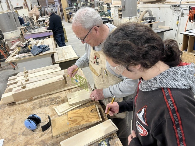A student is measuring wood with the help of a mentor.