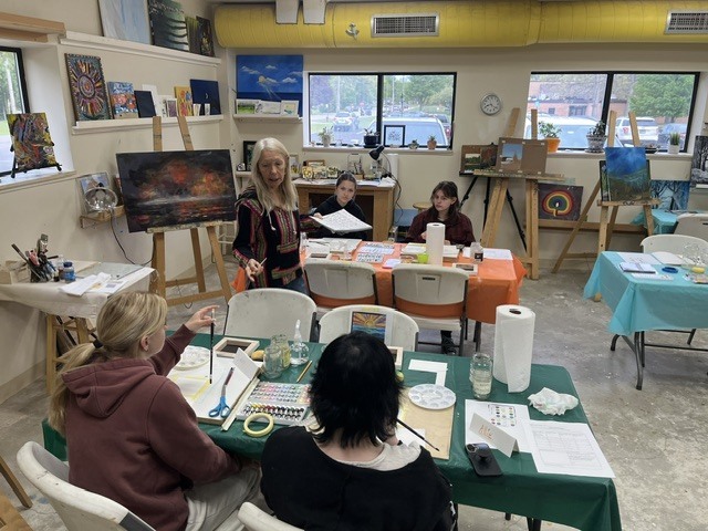 Miss Allie is giving painting instructions to 4 students.