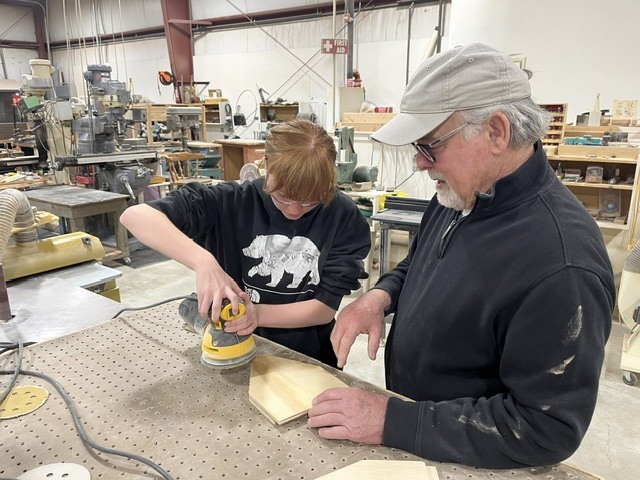A student is using a sander with a mentor supervising. 