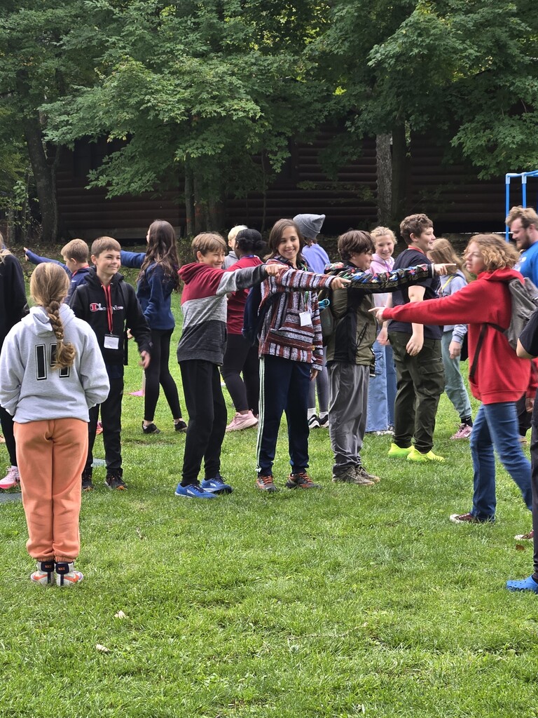 Middle Schoolers playing a game in a field and pointing at each other.