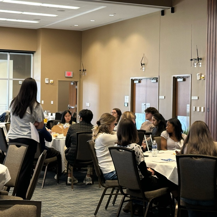small table of students seated and two facilitating students standing having a discussion