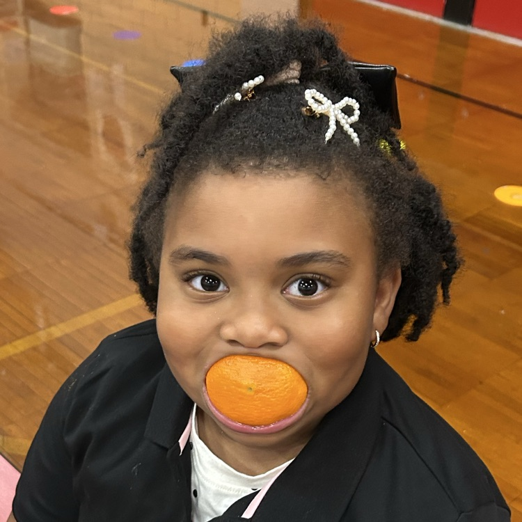 student with orange slice in mouth smiling