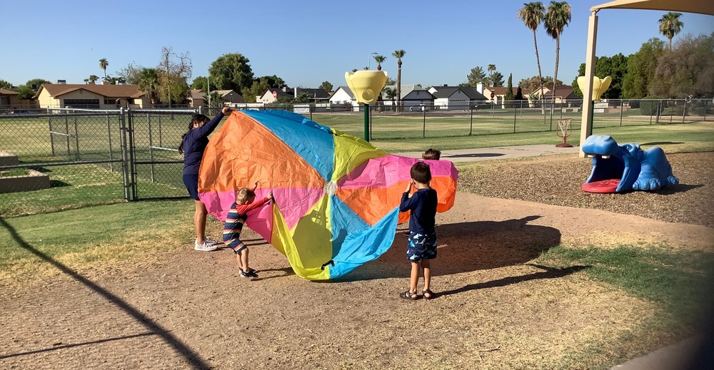 Preschool students playing outside with a large parachute