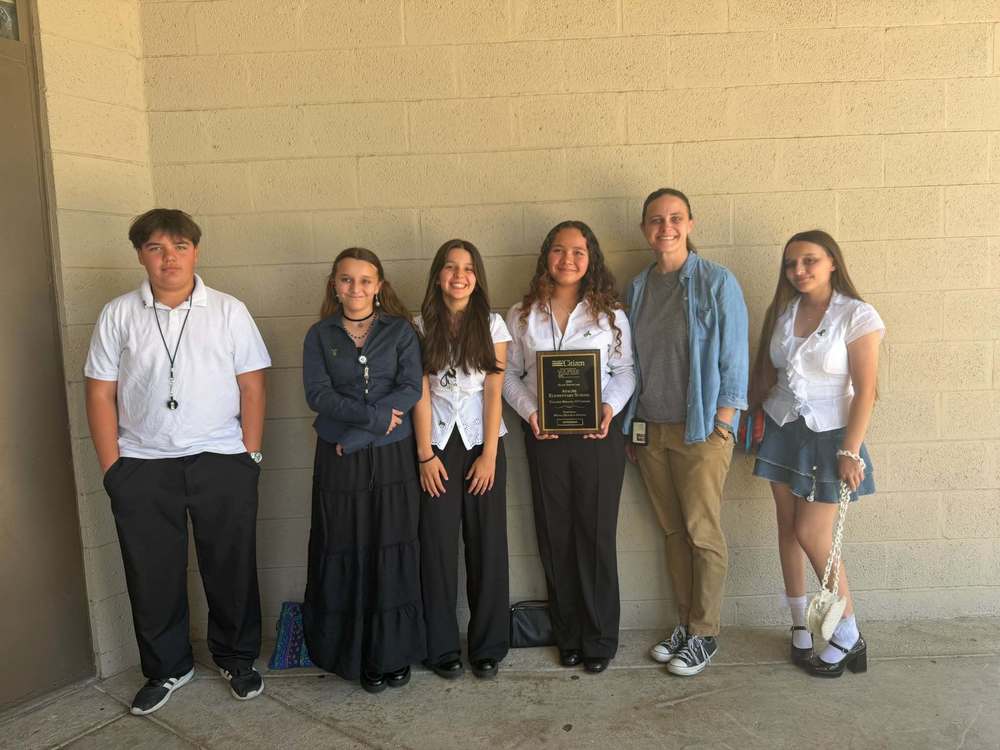 Students and Teacher pose against brick wall holding award.