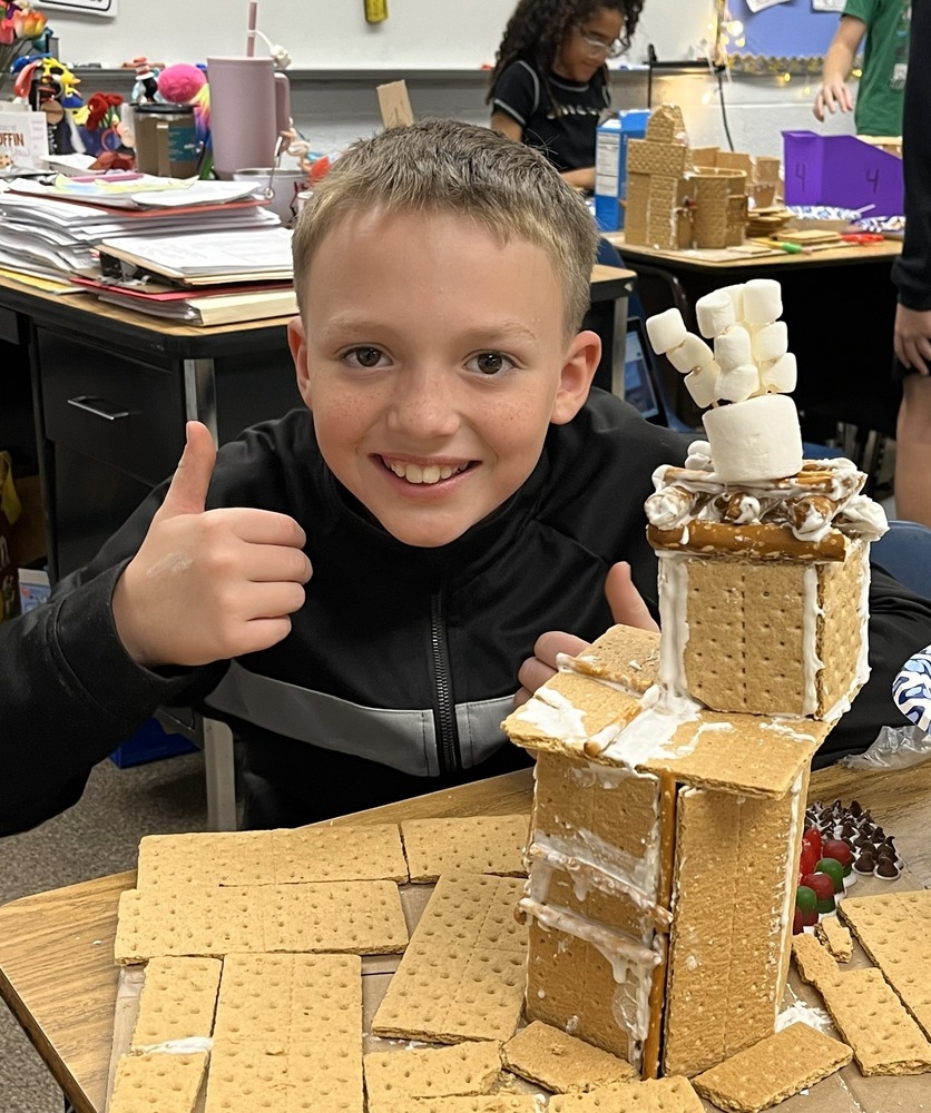 Male Student posing with thumb up behind his graham cracker house. 
