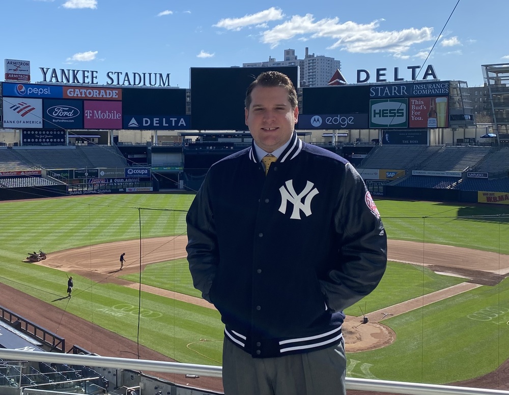 A male with a NY Yankees jacket on. The stadium is in the background.