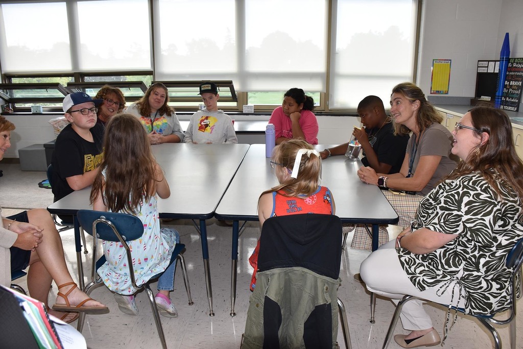 A group of elementary students and school personnel sitting together and talking. 