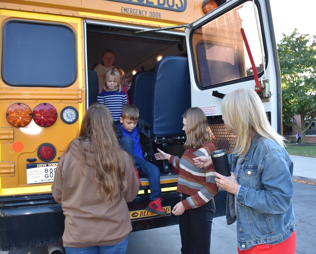 Two older students and an administrator helping younger students evacuate a school bus. 