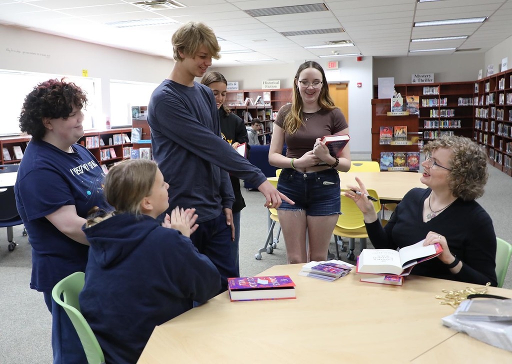 A female author having a discussion with five high school students.
