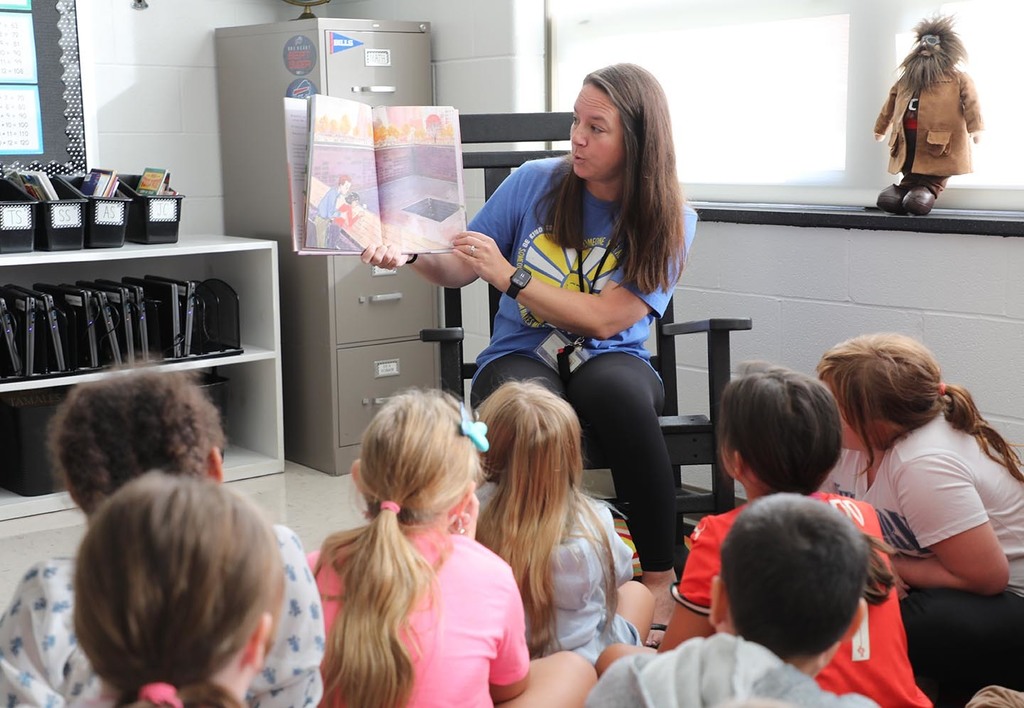 A female teacher reading a book to an elementary class. 