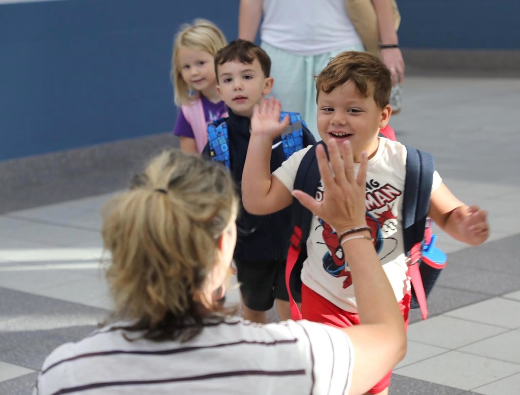Three elementary students give their principal high-fives. 