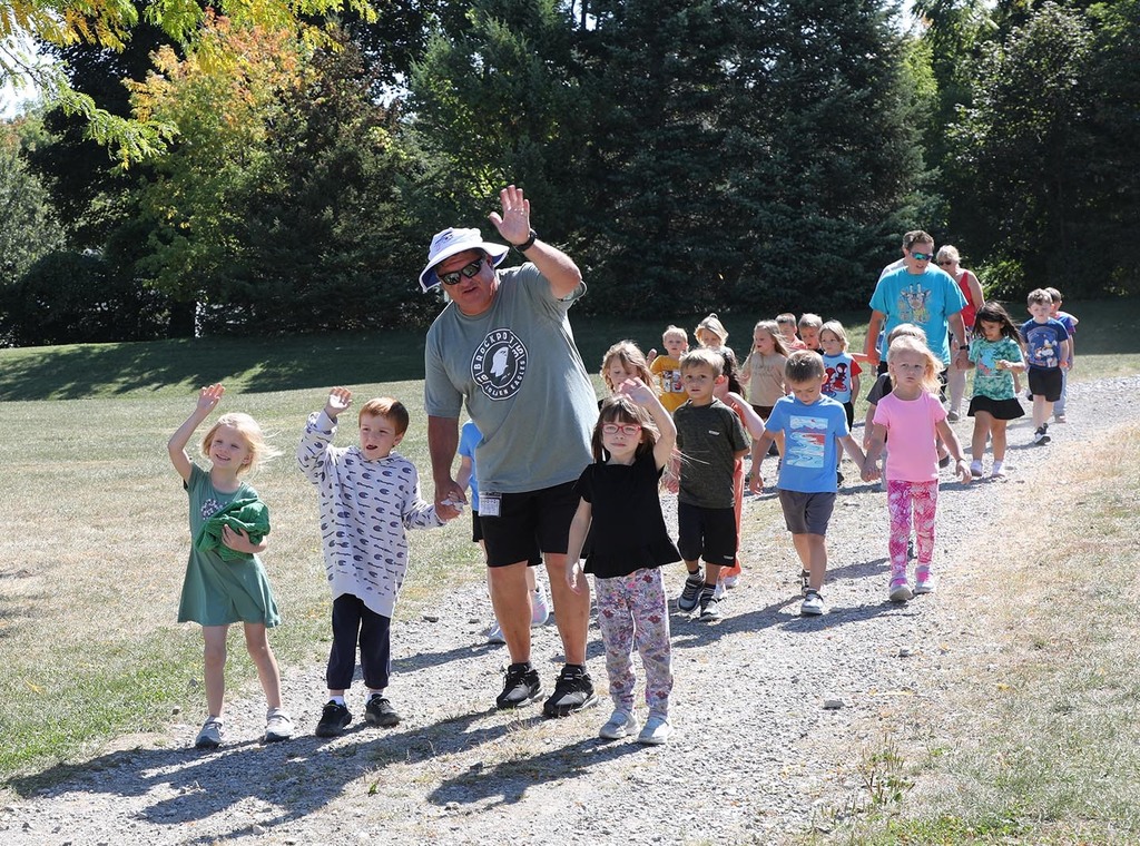 A group of elementary children and adults on a nature hike. Some are waving to the camera.