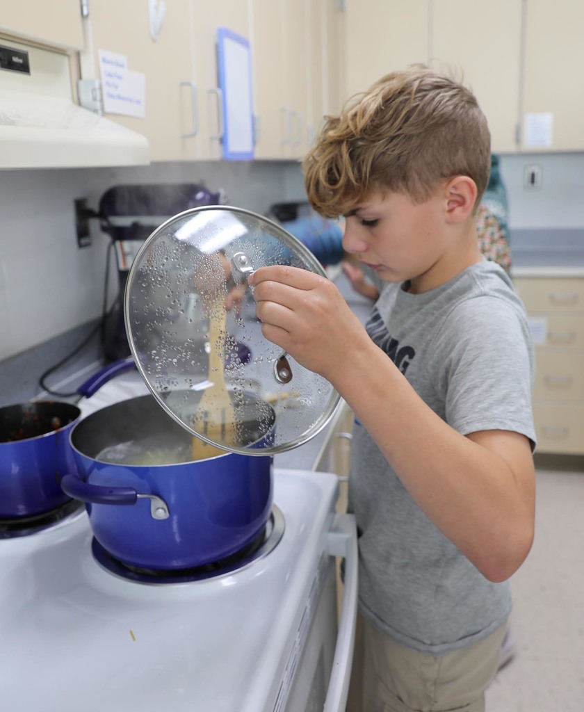 A JH student stirring pasta that is cooking on a stove. 