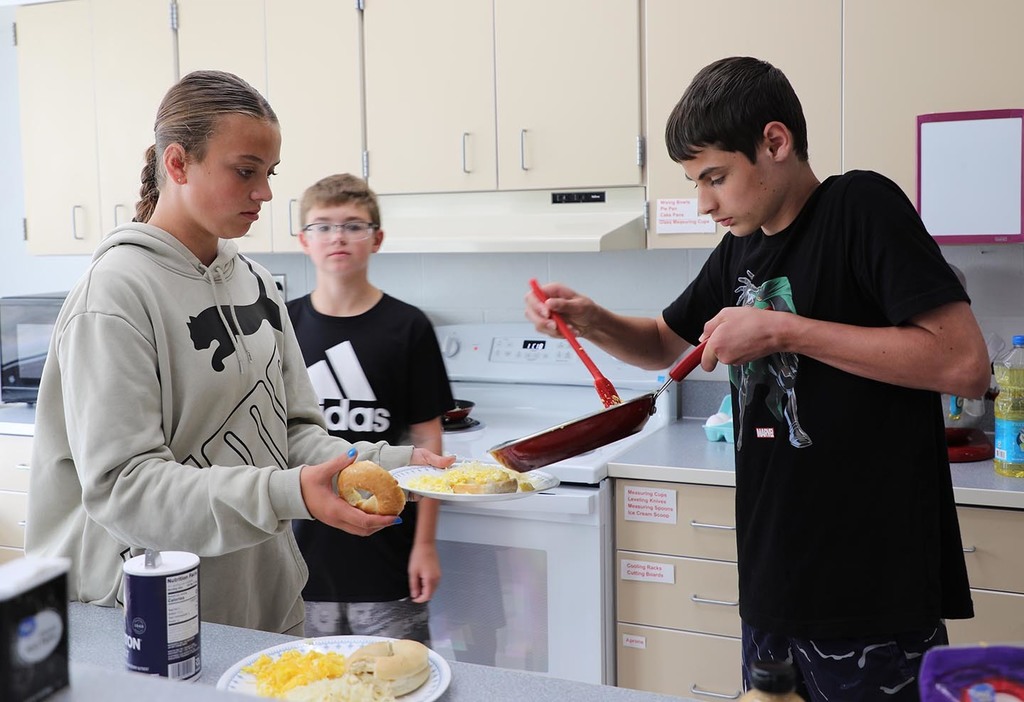 Two students cooking putting food on a plate, while another student watches. 