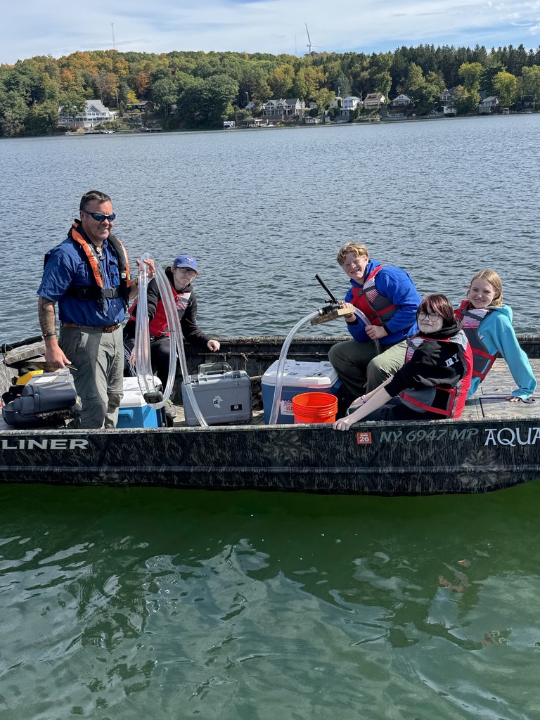 Four high school students and a teacher in a boat on water.
