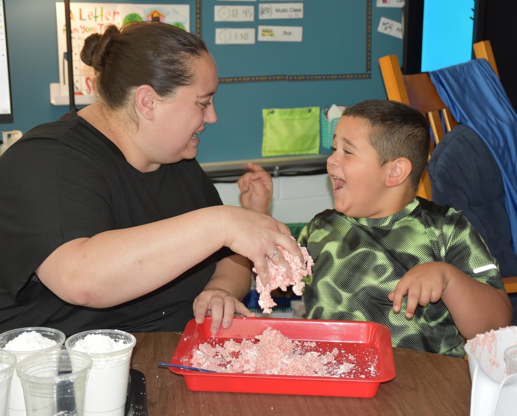 An elementary student smiling and pointing to the adult female sitting next to him.