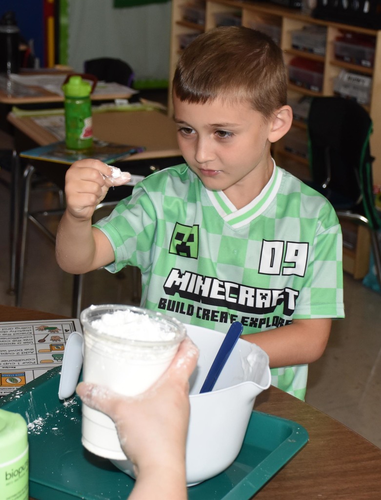A boy elementary student looking at his fingers, which are covered in flour. 