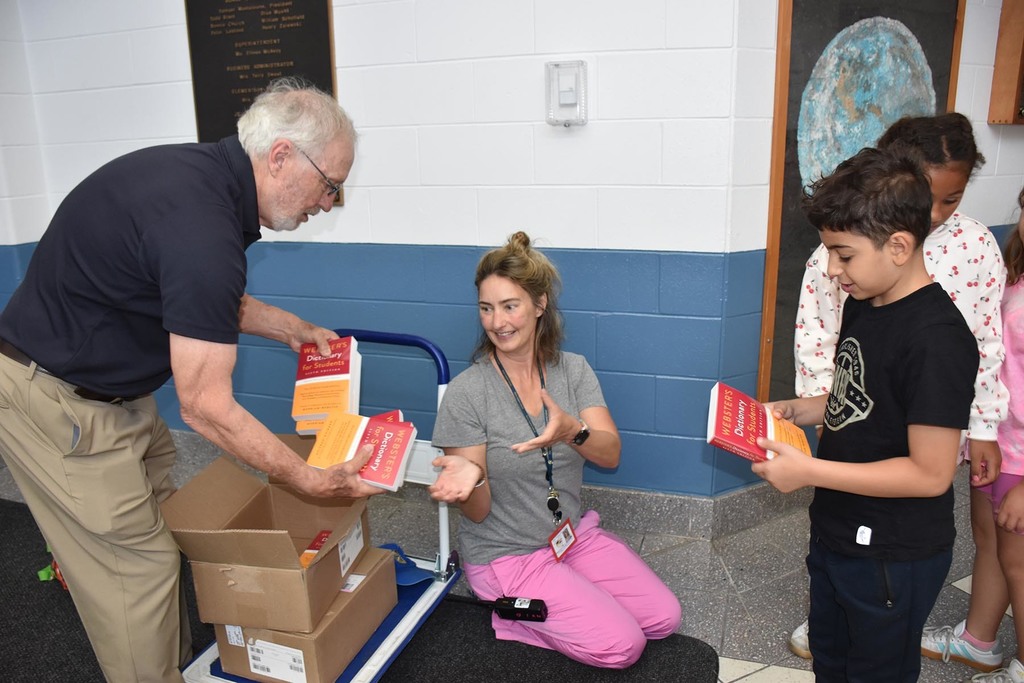 An adult male and adult female passing out dictionaries to elementary children. 