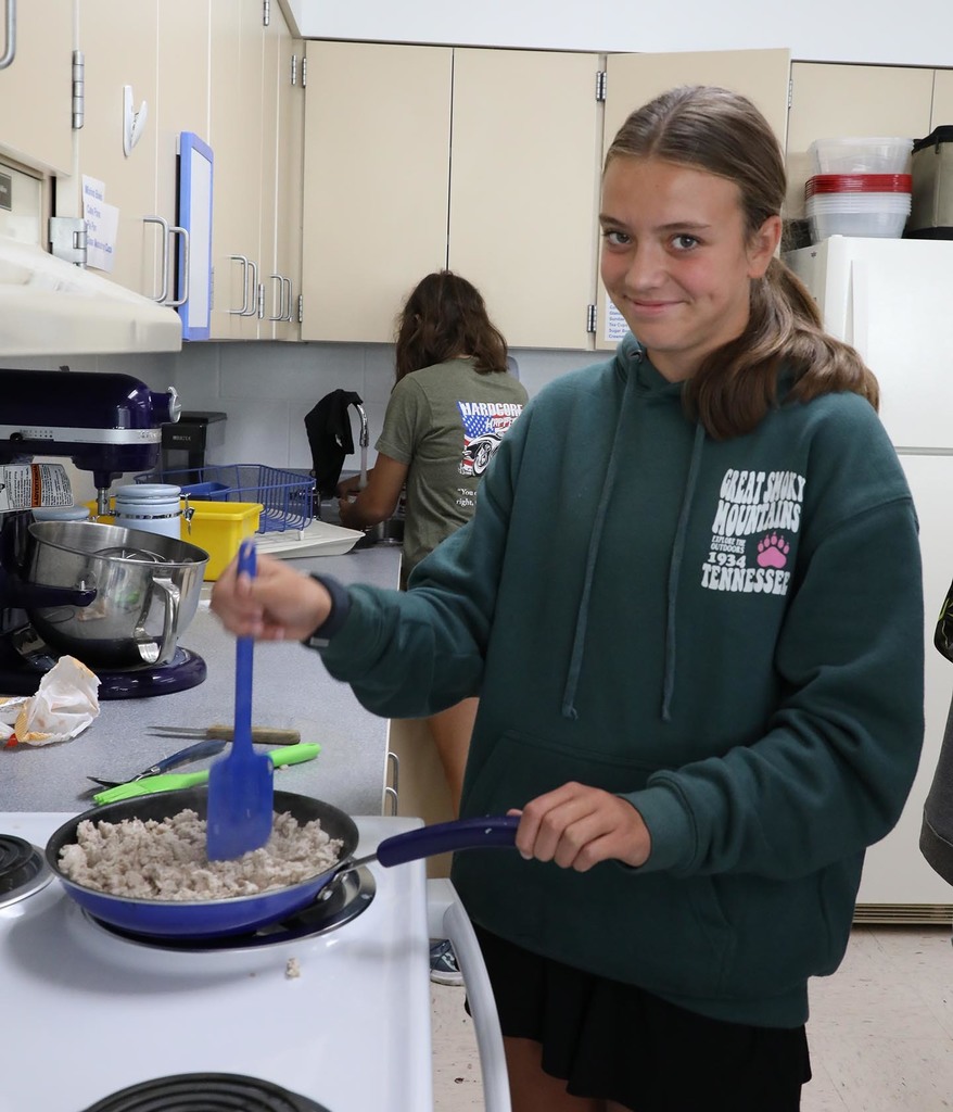 A jr. high girl cooking meat on a stove. 