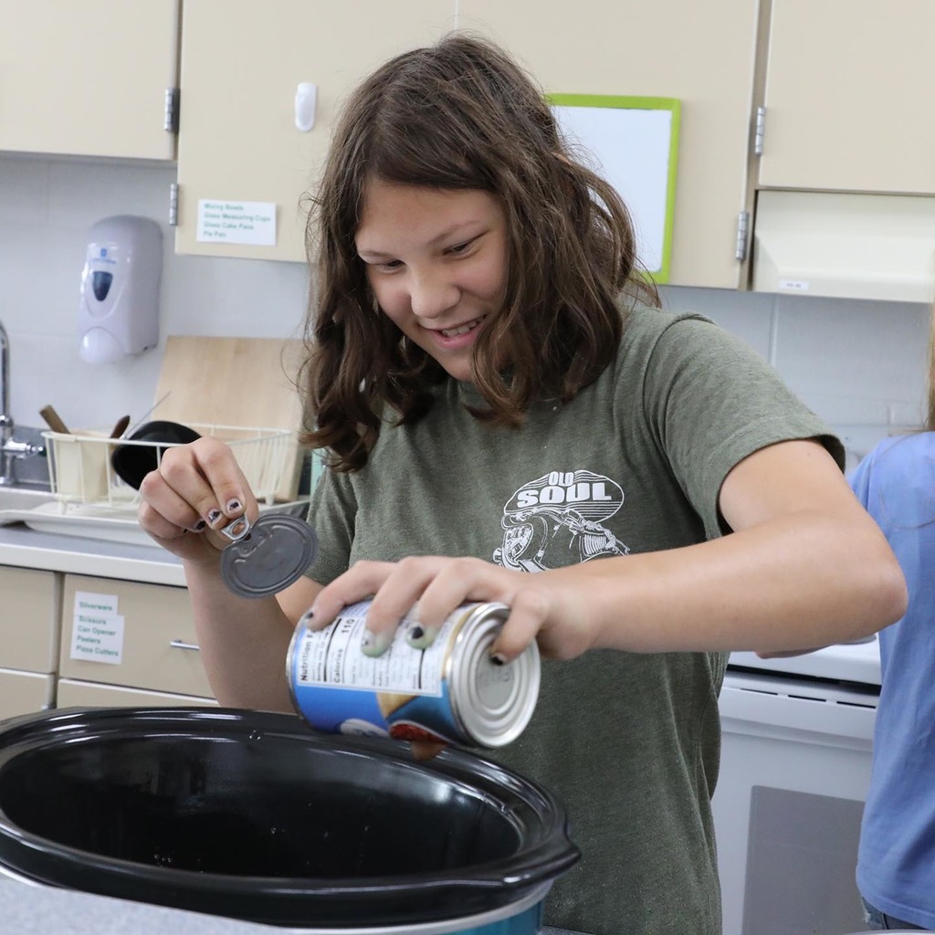 A Jr. High girl pouring beans into a crockpot. 