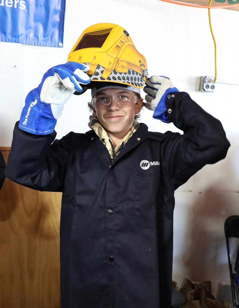 A high school boy wearing a welding jacket and helmet. 