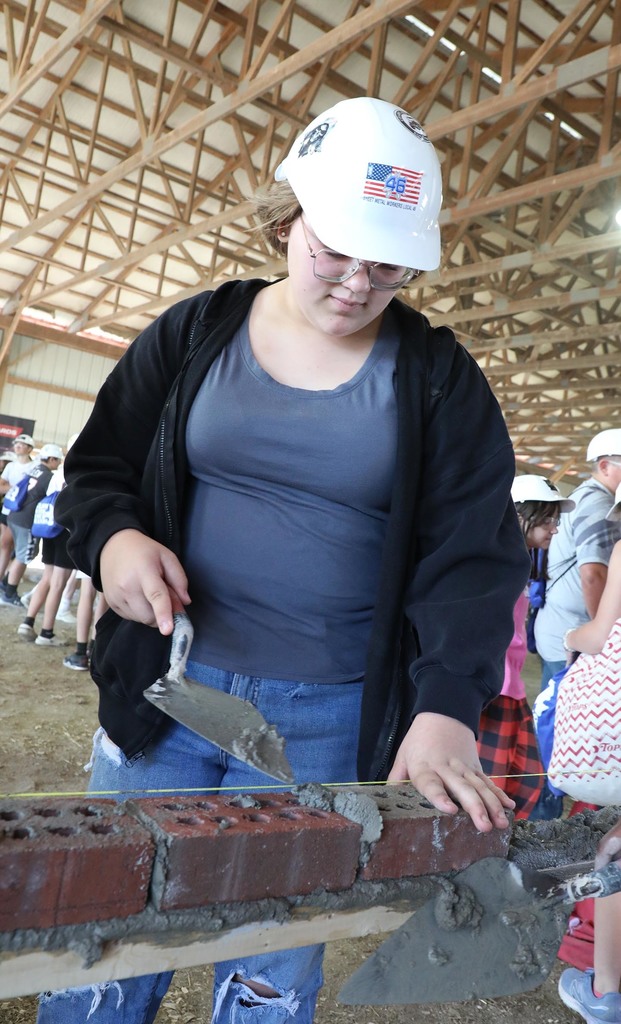A high school girl learning to lay bricks. 
