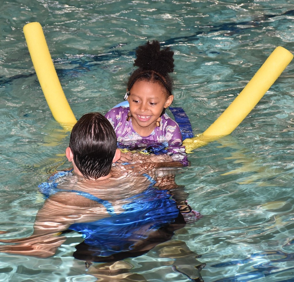 A young girl swimming in an indoor poor with an adult woman. 