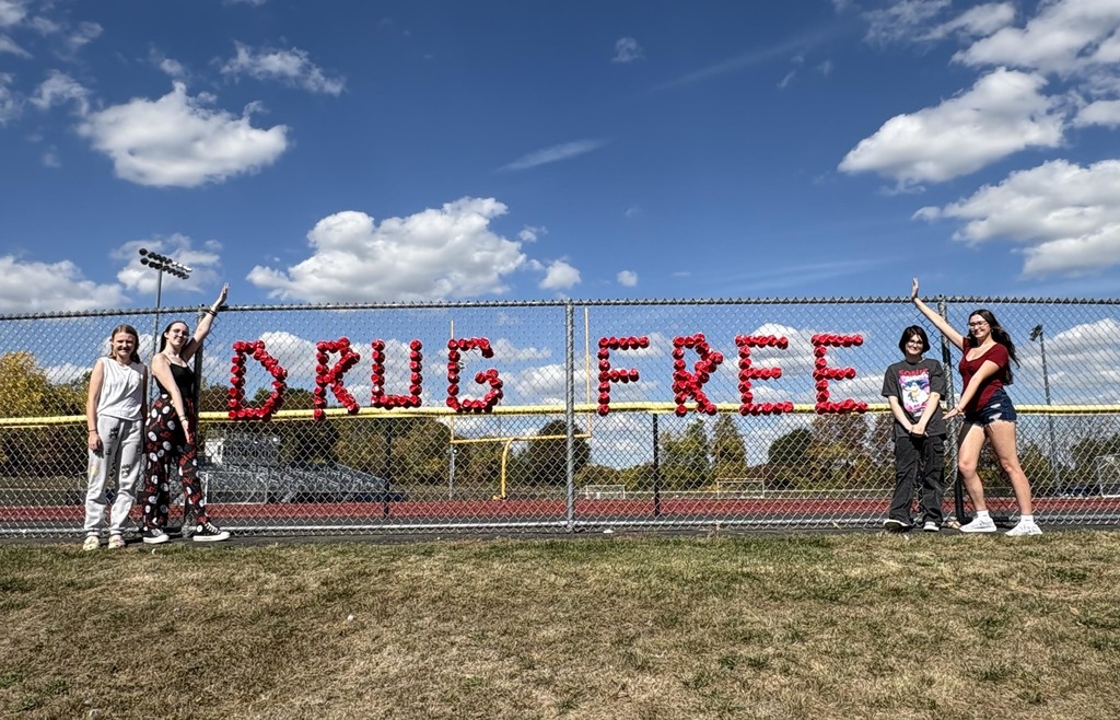 Four high school students standing by a fence sign that says "Drug Free."