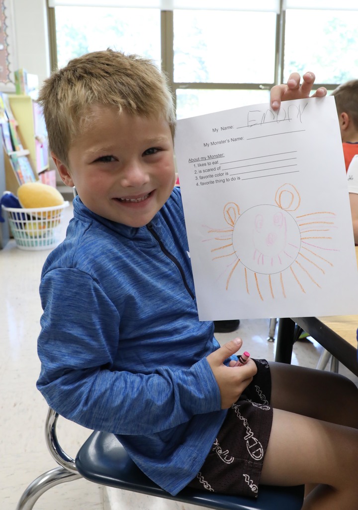 A kindergarten boy holding up a paper with a monster he drew. 