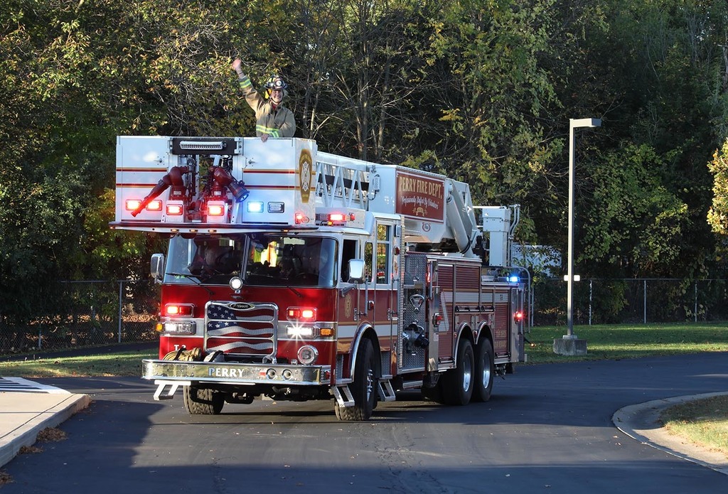 A person in the bucket of a fire truck, waving. 