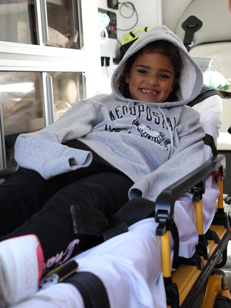 A young girl laying on a stretcher in an ambulance. She is smiling. 