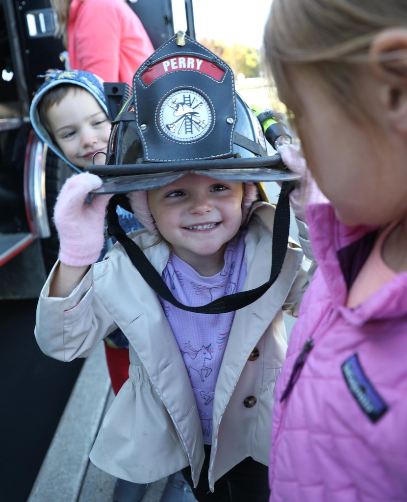 A young girl trying on a firefighter hat while others look on. 