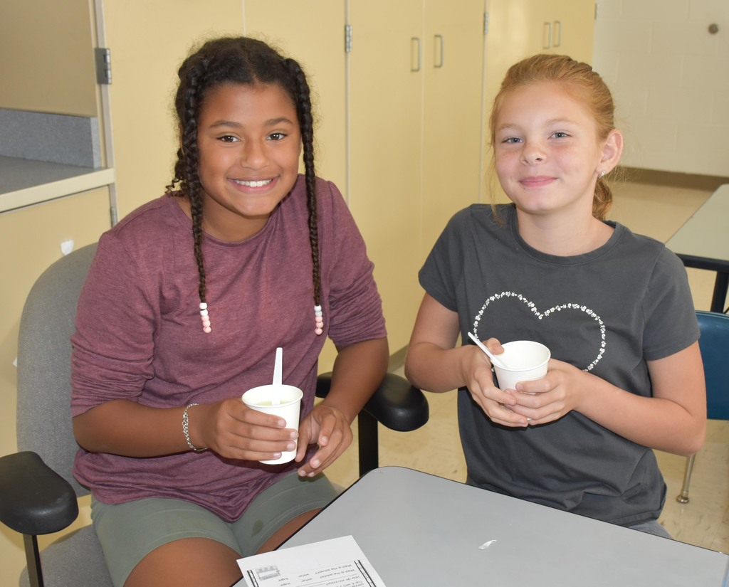 Two elementary students holding cups with spoons inside. 