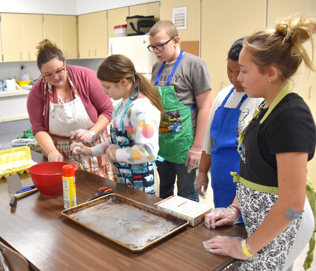 A female teacher helping four students bake brownies. 