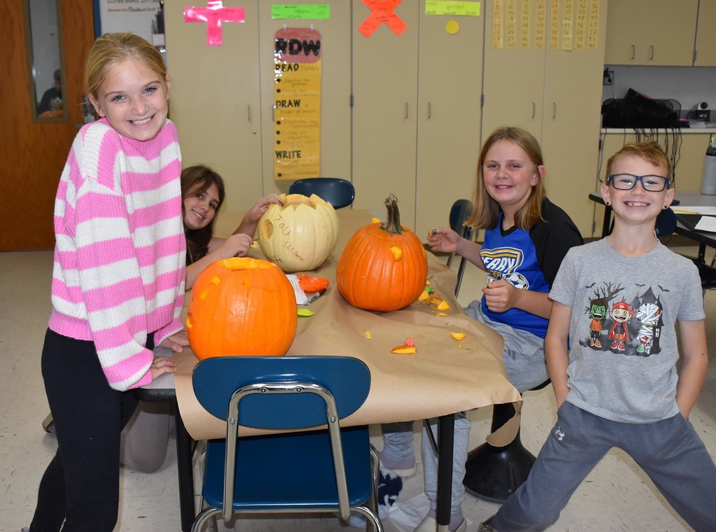 Four elementary students carving pumpkins. 