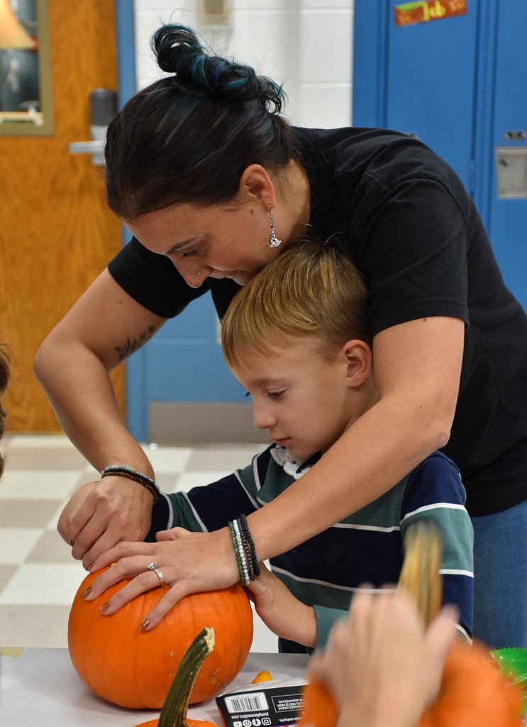 A woman helping a small children carve a pumpkin. 