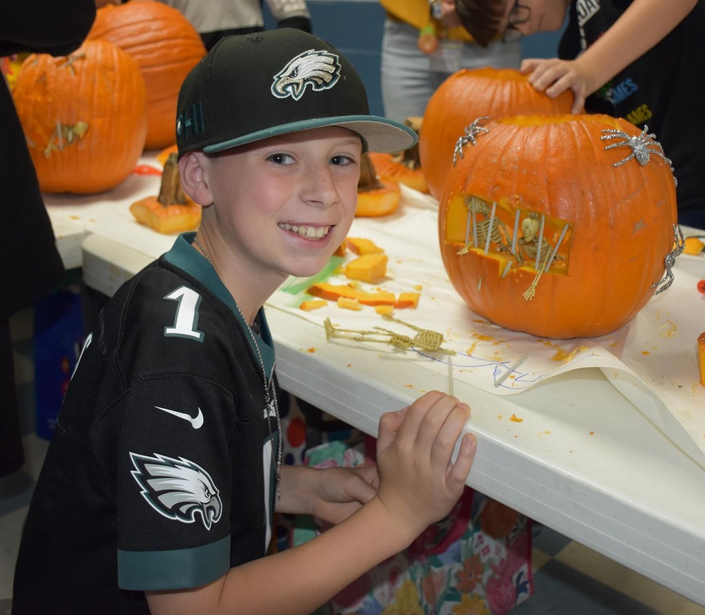 An elementary smiling by a pumpkin.