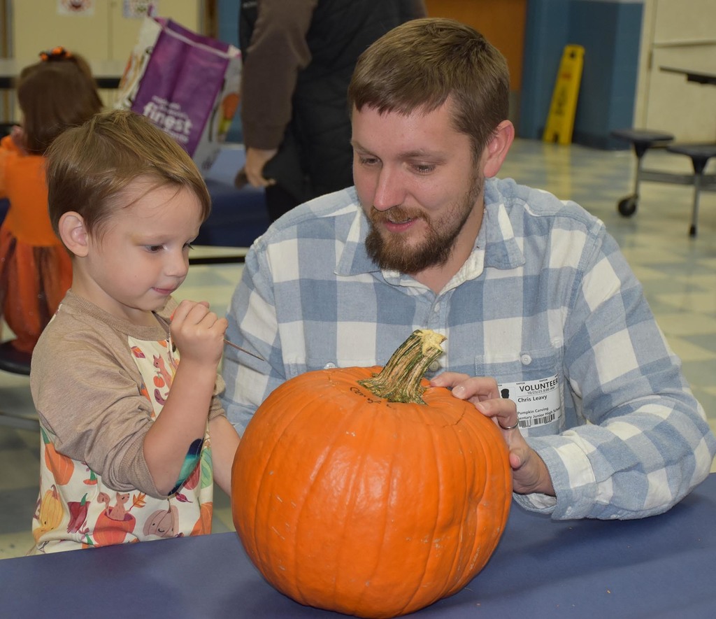 A father helping his young son carve a pumpkin. 