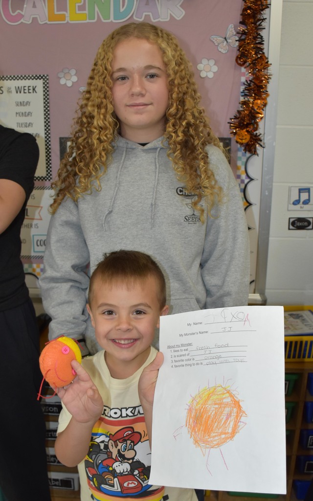 A junior high girl standing with a kindergarten boy. The boy his holding a paper and a stuffie. 