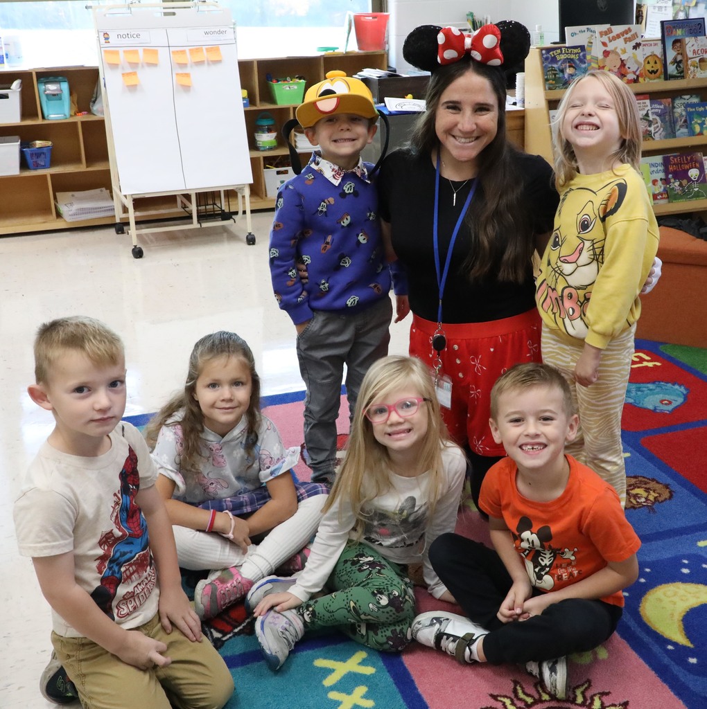 An adult female teacher posing with six kindergartners in a classroom. 