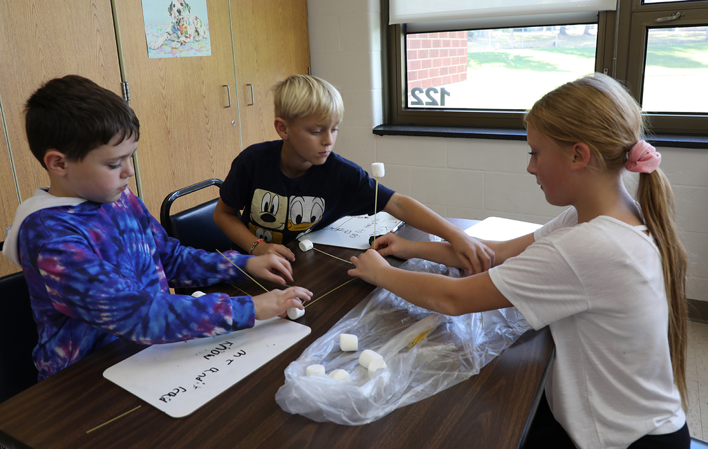 Three elementary students trying to build a tower with marshmallows and uncooked spaghetti. 