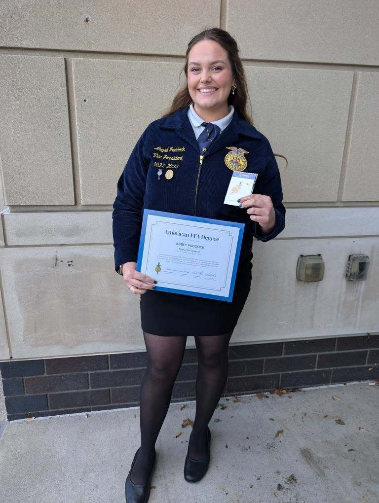 A female college student dressed in FFA formal attire, holding two certificates. 