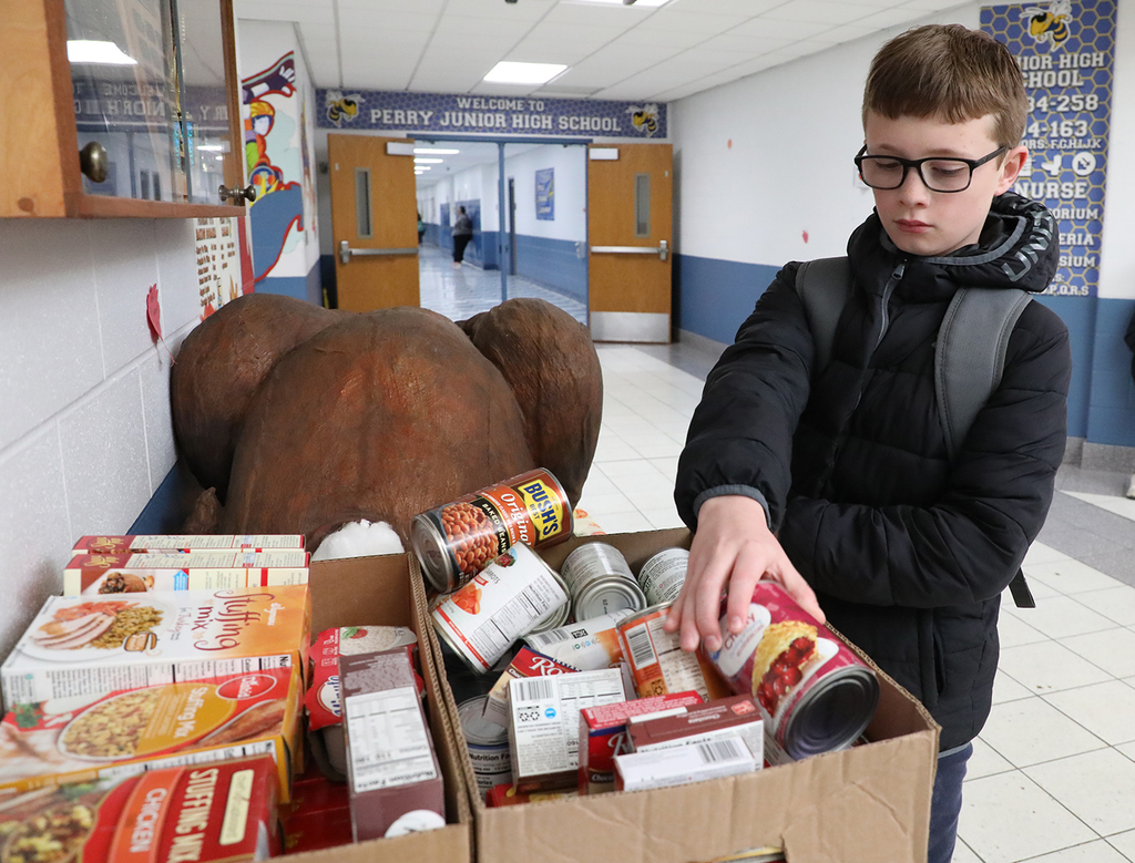 An elementary boy putting canned food in a box with other boxed and canned foods. 