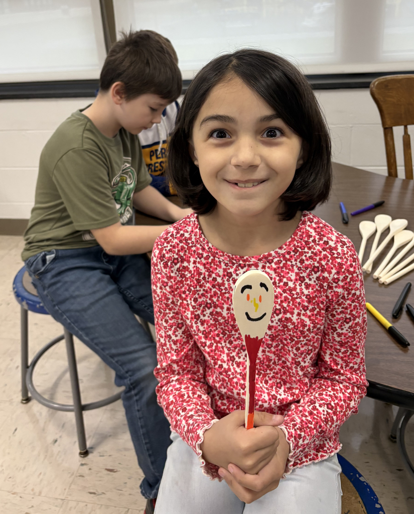 An elementary girl holding a wooden spoon that is decorated. Two boys are in the background. 