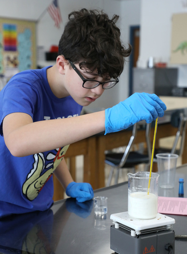A Jr. High boy conducting a science experiment in a classroom. 