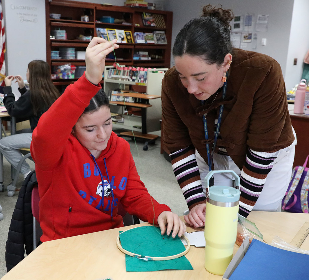 A female high school student receiving help from a female teacher with sewing. 