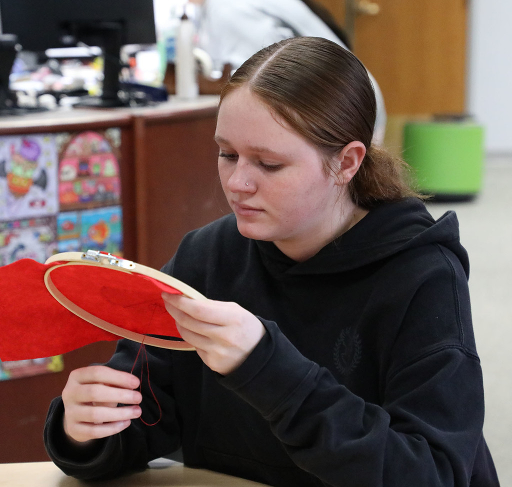 A female high school student sewing an ornament. 